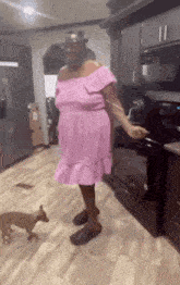 a woman in a pink dress is standing in a kitchen with a dog .