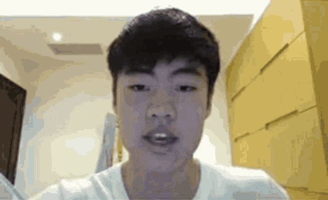 a young man in a white shirt is looking at the camera and making a funny face .
