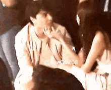 a man and a woman are sitting next to each other in a crowd and the man is licking the woman 's hand .