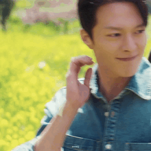 a man wearing a denim shirt is standing in front of a field of yellow flowers .
