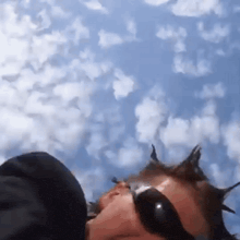 a person wearing sunglasses looks up at a cloudy sky