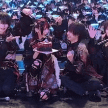 a group of people are kneeling down on a stage holding a cake in front of a crowd .