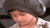 a young boy wearing a gray hat and a white shirt looks down at something