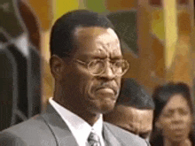 a man in a suit and tie is standing in front of a crowd and making a funny face .