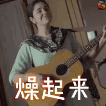 a woman is playing an acoustic guitar in a room with chinese writing behind her