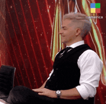 a man in a suit and tie is sitting in front of a red curtain and smiling ..