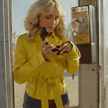 a woman in a yellow jacket talking on a payphone