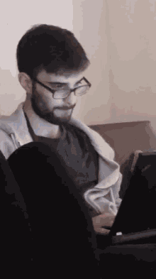 a man with a beard and glasses is sitting in front of a laptop computer .
