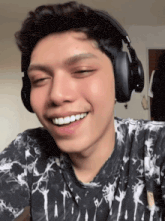 a young man wearing headphones and a tie dye shirt smiles with his eyes closed
