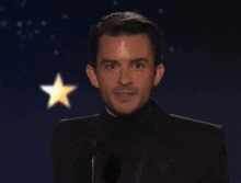 a man in a suit stands in front of a microphone with a star in the background
