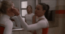 a woman applying makeup to another woman in front of a mirror