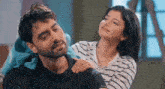 a man and a woman are sitting next to each other and the woman is putting her hand on the man 's neck .