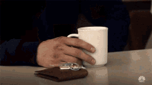 a man is sitting at a table with a cup of coffee and a wallet with keys on it .