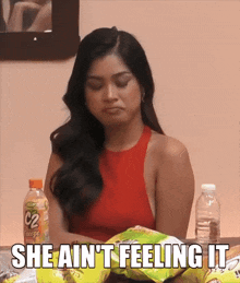 a woman sitting at a table with a bag of chips and the words she ain t feeling it