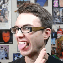 a young man wearing glasses is sticking his tongue out in front of a wall with cars posters