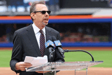 a man in a suit stands at a podium with two microphones that say citi