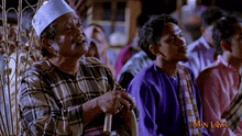 a man in a plaid shirt sits next to another man in a purple shirt with the words man laksa on the bottom