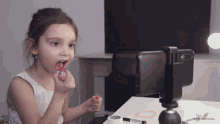a little girl applying lipstick in front of a phone