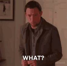 a man in a jacket is standing in a room and asking what ?