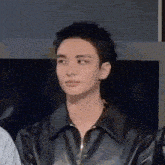 a young man wearing a black leather jacket is standing in front of a television .
