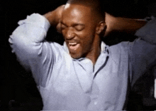 a man in a blue shirt is holding his hands behind his head .