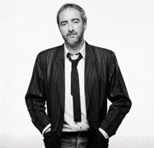 a man with a beard wearing a suit and tie with his hands in his pockets