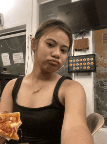 a woman in a black tank top holds a slice of pizza in front of a sign that says no smoking