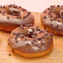 three chocolate glazed donuts with chocolate chips on a wooden cutting board