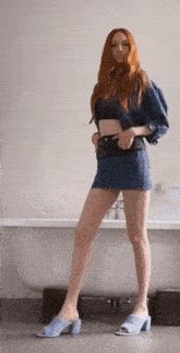 a woman is standing in front of a bathtub wearing a denim skirt and blue mules .