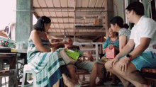 a group of people are sitting on a porch with a man holding a gift box