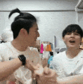 two young men are standing next to each other in a room . one of the men is wearing a ponytail .