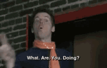 a man wearing an orange scarf and a blue shirt says " what are you doing "