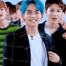 a man with blue hair is smiling and holding a microphone while standing next to another man .