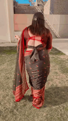 a woman in a black and red saree is standing in a grassy yard .