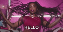 a woman with dreadlocks is dancing in front of a pink background and saying hello .