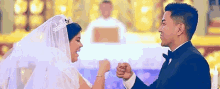 a bride and groom are holding hands in front of a priest in a church .
