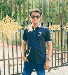 a man wearing sunglasses and a tesla shirt stands in front of a gate