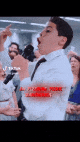 a boy in a white shirt and tie is singing into a microphone in front of a crowd of people .