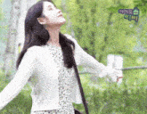 a woman with her arms outstretched is wearing a white sweater and a floral dress