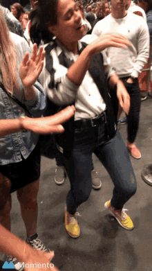 a woman is dancing in a crowd with a momento icon in the corner