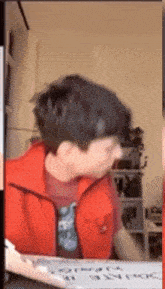 a man wearing a red vest is sitting at a table with a white board that says " gracias " on it