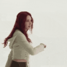 a woman with red hair is dancing in a white jacket and crop top .