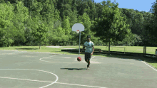 a man dribbles a basketball on a court with trees in the background