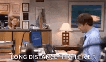 a man is sitting at a desk in front of a computer with the words `` long distance high five '' written above him .