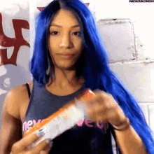 a woman with blue hair is holding a bottle of orange juice in her hand .