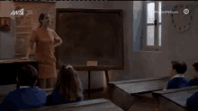 a woman stands in front of a blackboard in a classroom with a clock on the wall that reads 12