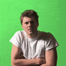 a man in a white shirt is standing with his arms crossed in front of a green screen .