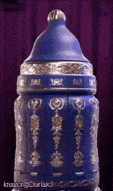 a blue bottle with gold decorations and a purple curtain behind it .
