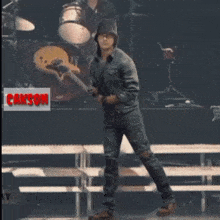 a man is standing on a stage with a drummer in the background and the word caxson in the corner