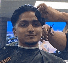 a man is getting his hair cut by a barber wearing a black cape that says ' shop ' on it